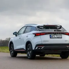 Białe, nowoczesne chinskie auto OMODA 5 z charakterystycznym pasem świateł z tyłu, zaparkowane na poboczu drogi.