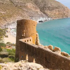 Ruinas de un antiguo torreón y murallas de piedra junto a una cala de aguas turquesas. Un lugar con historia que ver en Las Negras, Almería.