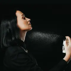 Kobieta rozpyla wodę toaletową na szyję, tworząc mgiełkę zapachu. Dowiedz się, jak używać wody toaletowej, by podkreślić swoją elegancję.