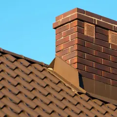 Ziegel-Schornstein auf braunem Ziegeldach vor blauem Himmel. Überlegungen, den alten Schornstein stilllegen zu lassen, sind im Gange.