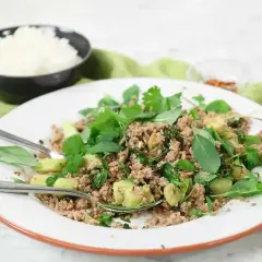 En tallrik med kycklingfärs, färska örter och grönsaker, perfekt för ett snabbt larb recept. Ris i bakgrunden.