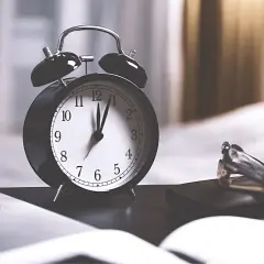 Budzik pokazuje 12:00. Ile minut trwa rozprawa w sądzie? Czas biegnie, a na biurku leżą dokumenty i długopisy.
