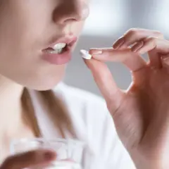 Kobieta bierze tabletkę clindamycin mip 600, trzymając ją palcami i szklankę wody.