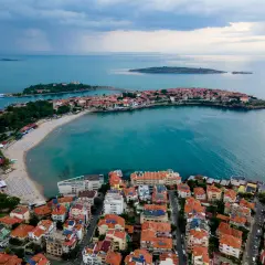 Bułgaria jakie morze? Widok z lotu ptaka na malowniczą zatokę z piaszczystą plażą, urokliwe miasteczko z czerwonymi dachami i turkusowe wody Morza Czarnego.