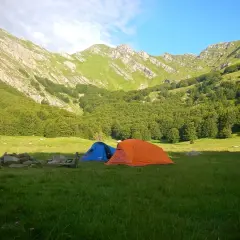 Tende da campeggio in un prato verde, con montagne boscose sullo sfondo, vicino alle sorgenti del Secchia.
