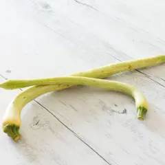 Due zucchine trombetta, lunghe e curve, giacciono su un tavolo di legno chiaro.