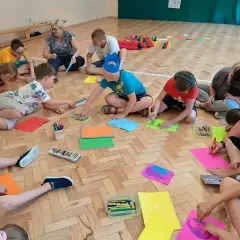 Dzieci klas 1-3 biorą udział w zabawach integracyjnych, rysując i kolorując na podłodze.