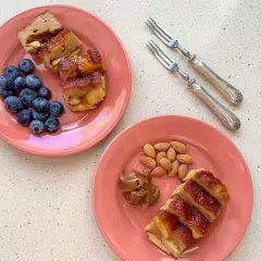 Dos platos rosados con porciones de pudin de manzana, arándanos y almendras. Un postre casero para disfrutar.