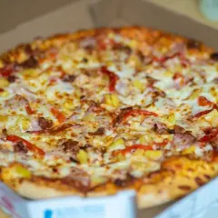 Pyszna pizza hawajska w pudełku, idealna do odgrzania w mikrofali. Ser, szynka i ananas kuszą swoim wyglądem.