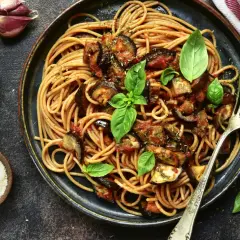Assiette de pâtes à l'italienne, spaghetti avec aubergines et sauce tomate, garnie de basilic frais. Ail et parmesan à côté.