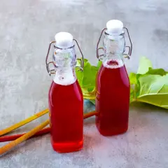 Dwie butelki z rubinowym sokiem z rabarbaru, obok łodygi i liście rabarbaru.