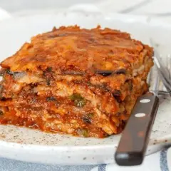 Porción de pastel de berenjenas, con capas de berenjena y salsa de tomate, servido en un plato blanco con cubiertos. ¡Un pastel de berenjenas facilisimo!
