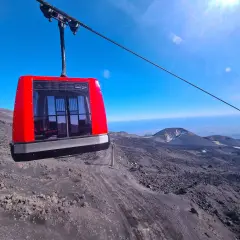 Cabina rossa della funivia in viaggio verso l'altezza Etna Rifugio Sapienza, su un paesaggio lunare di rocce laviche.