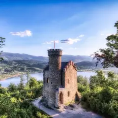 Kamienny zamek na wzgórzu, otoczony zielenią, z widokiem na jezioro i góry. To jedne z pięknych walorów przyrodniczych Polski.
