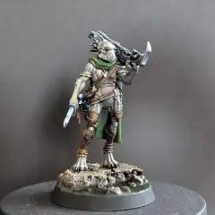 Zbrojny kroot w zielonej pelerynie i brązowych ochraniaczach, z nożem w dłoni i karabinem na plecach, gotowy do walki.