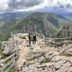Dos personas admiran el paisaje montañoso desde el mirador del Cerro del Viso. El cielo está nublado.