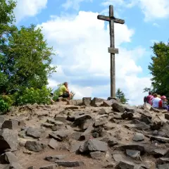 Kamienisty szczyt z drewnianym krzyżem i grupą turystów.