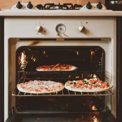 Trois pizzas cuisent dans un four. Le réglage de la température cuisson pizza est visible sur le panneau.