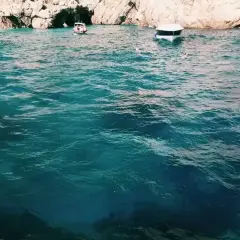 Acqua cristallina e turchese vicino all'ingresso di una grotta, con barche e bagnanti che godono della bellezza della Grotta Azzurra.