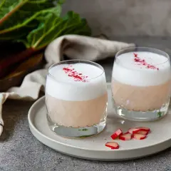 Två glas med en krämig rabarber sour, toppad med skum och strödd med torkad rabarber.
