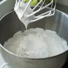 Masa z mascarpone, puszysta i biała, spływa z mieszadła miksera do metalowej misy.