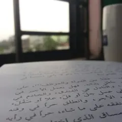 Otwarta księga z tekstem w języku arabskim, obok kubek i widok przez okno.