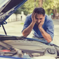 Zrozpaczony mężczyzna patrzy na otwartą maskę samochodu. Jego auto nie odpala, a on nie wie, co robić.