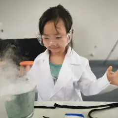 Niña con bata de científico y gafas experimenta con humo, ¡geniales inventos para niños de 6 a 8 años!
