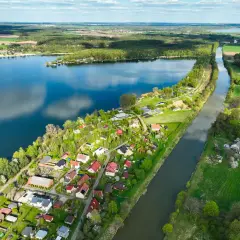 Malownicze jezioro Pławniowice otoczone zielenią i domkami letniskowymi, z kanałem wodnym biegnącym wzdłuż brzegu.