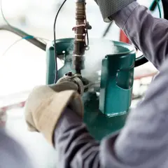 Pracownik w rękawicach obsługuje zawór butli z gazem, z której wydobywa się para. To kluczowy moment w procesie kontroli temperatury spalania propan butan.