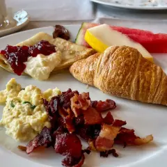 En härlig **continental frukost** med krämiga äggröror, knaprigt bacon, en croissant, pannkakor med sylt och grädde, samt färsk frukt.