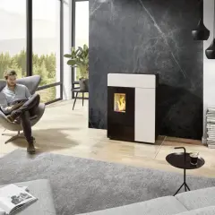 Un homme lit dans un fauteuil près d'un poêle moderne. Le **carrelage derrière le poêle** en marbre noir crée un contraste saisissant.