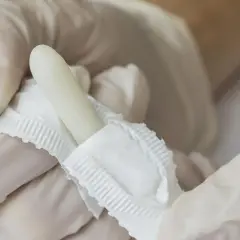 Ręce w białych rękawiczkach trzymają biały czopek.