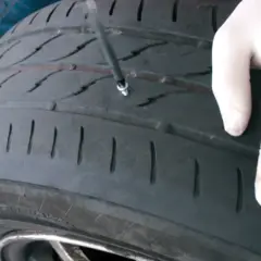 Mano enguantada inserta herramienta para reparar pinchazo. Es seguro reparar un pinchazo si se hace correctamente.
