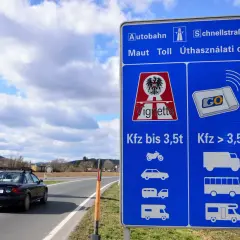 Znak informuje o opłatach za autostrady w Austrii. Widoczny jest samochód na drodze i niebieski znak z symbolami pojazdów.