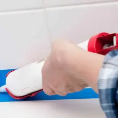 Application d'un joint époxy pour douche, avec du ruban bleu pour un résultat net.