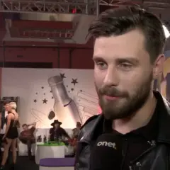 Ernest Staniaszek udziela wywiadu na tle scenografii z butelką i gwiazdami.