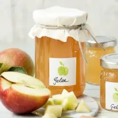 Zwei Gläser mit selbstgemachtem Apfelgelee, daneben frische Äpfel und gewürfelte Apfelstücke. Ein leckeres Apfelgelee Rezept zum Nachmachen.