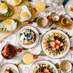 Un festin de brunch : toasts à l'avocat et œuf au plat, gaufres aux fruits rouges et myrtilles, jus d'orange et café.