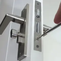 Réparation d'une poignée de porte qui claque avec le vent. Un tournevis ajuste la serrure.