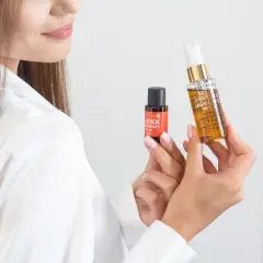 Kobieta prezentuje dwa kosmetyki do włosów, pokazując jak używać serum do włosów z olejkiem arganowym dla pięknych i zdrowych pasm.