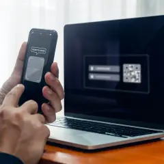 Ręce trzymają telefon z napisem "SCAN TO LOGIN", obok laptop z kodem QR. Szybkie logowanie, jak zeskanować kod na telefon.