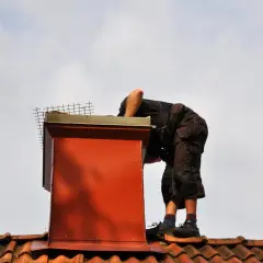Pracownik na dachu sprawdza komin. Dowiedz się, ile kosztuje naprawa komina na dachu, gdy wymaga prac wysokościowych.