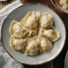 Talerz pełen pierogów z kapustą i grzybami, obok miseczka z przyprawami i kapustą kiszoną.