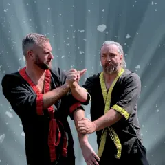 Två män i traditionella dräkter tränar wing chun. Ljuset strålar bakom dem.