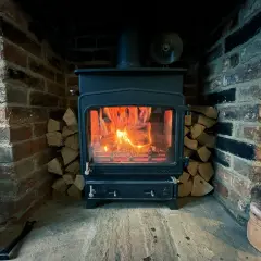 Poêle à bois allumé dans une cheminée en briques, avec du bois empilé. La **réglementation tubage poêle à bois** assure une évacuation sûre des fumées.