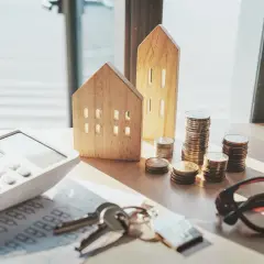 Drewniane domki, stosy monet i kalkulator sugerują planowanie finansowe. Ile procent wkładu własnego będzie potrzebne na wymarzone mieszkanie?