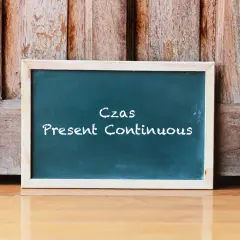 Tablica z napisem "Czas Present Continuous" na tle drewnianych drzwi. Uczysz się, co to jest present continuous?