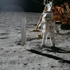 Astronaut na Księżycu podczas misji Apollo, obok lądownika. W tle amerykańska flaga.