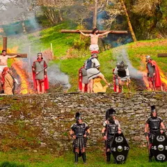 Recreación de la crucifixión en Semana Santa en Asturias. Hombres vestidos de romanos y figuras crucificadas en un paisaje verde.